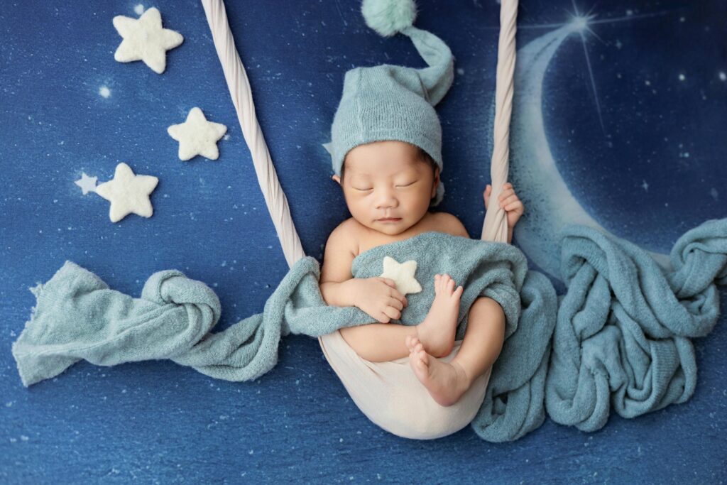 Cute newborn sleeping peacefully in a cozy, starry bed setup, wrapped in teal blankets.